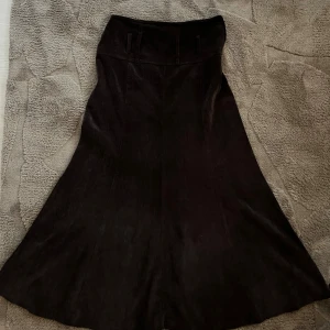 Brun manchesterkjol från Şahinler Tekstil - Säljer en brun långkjol i manchester från Şahinler Tekstil. Kjolen har hög midja, bälteshällor och dragkedja i sidan. Den har en lätt utsvängd form som ger en snygg siluett och passar perfekt till chunky boots eller sneakers.