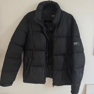 Svart pufferjacka från Zara  - Svart pufferjacka från Zara i storlek XL. Jackan har hög krage, dragkedja framtill och två sidofickor. Quiltad design med diskret dnwr.-patch på ena ärmen. Perfekt för kalla dagar och enkel att matcha med allt.