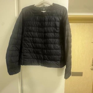 Svart dunjacka från Uniqlo, S - Lätt och smidig svart dunjacka från Uniqlo Ultra Light Down. Jackan har rund halsringning, tryckknappar framtill och quiltad design. Perfekt för lager-på-lager och enkel att bära med sig. Snygg minimalistisk look som funkar till det mesta.