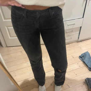 Svarta raka jeans med slitning - Svarta Levi’s jeans med slitning vid knäet. Klassisk femficksmodell med knapp och dragkedja. Jeansen har låg midja och bootcut modell💓storlek 28x34