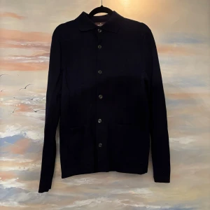 Mörkblå overshirt från Morris merinoull - Snygg mörkblå kofta/overshirt från Morris i storlek XS. Koftan har klassisk krage, knäppning med knappar framtill och två fickor. Tillverkad i mjukt stickat merinoull som passar perfekt till lager-på-lager-stil. Nypris 3100kr. Sparsamt använd, fint skick. 