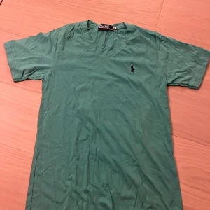 Grön v-ringad t-shirt från Polo - Snygg grön t-shirt från Polo med v-ringning och klassisk broderad logga på bröstet. T-shirten är i 100% bomull och har korta ärmar. Perfekt för dig som gillar enkel och stilren design.