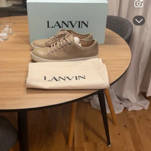 Beige sneakers från Lanvin i mocka - Snygga beige sneakers från Lanvin med ovandel i mocka och detaljer i skinn. Skorna har rund tå, platt vit sula och matchande beige snörning. Perfekta för dig som gillar stilrena och exklusiva sneakers. Kommer med originalkartong och dustbag. Finns några enstaka skavanker som skadan på sidan av skorna men ingen man tänker på. Pris kan diskuteras! 