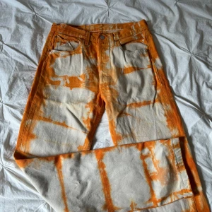 Levi's 501xx orange tie-dye jeans - Unika Levi's 501xx jeans med orange och vita tie-dye-effekter. Klassisk rak passform, femficksmodell och knappgylf. Jeansen är i kraftig bomull och har en riktigt cool vintage-vibe. Perfekta för dig som vill sticka ut med färg och mönster. Strl L/ W32 L36