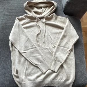 Beige cashmir hoodie  - Säljer en stilren beige hoodie med huva och snörning. Tröjan har långa ärmar och ribbade muddar vid ärmslut och nederkant. Perfekt för en chill och avslappnad look.