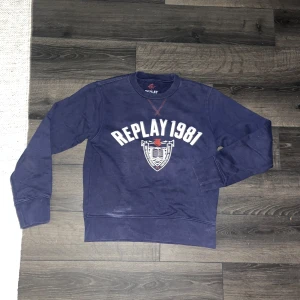 Replay tröja  - Säljer en marinblå sweatshirt från Replay med trycket 'REPLAY 1981' och ett coolt emblem framtill. Tröjan har rund hals, långa ärmar och ribbade muddar. Perfekt för dig som gillar klassisk streetstyle och vill ha något bekvämt och snyggt. Som det syns har tröjan en blekning/fläck långt ned till vänster på framsidan.OBS! Tröjan har möjligen krympt i tvätten så kolla måtten noggrant. 