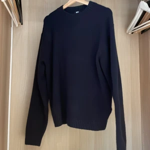 Mörkblå stickad tröja med rund hals - En stilren mörkblå stickad tröja med rund halsringning och långa ärmar. Tröjan har ribbade muddar vid ärmslut och nederkant, perfekt för lager på lager under kyliga dagar.