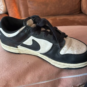 Nike Dunk Low svart/vit sneaker - Nike Dunk Low sneakers i svart och vitt skinn med klassisk swoosh på sidan. Lågt skaft, svarta snören och perforerad tåbox för extra ventilation. Tjock vit sula med svart yttersula. Perfekt för dig som gillar retrostil och streetwear.