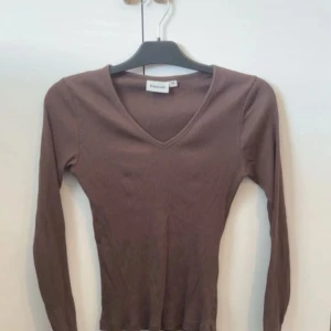 Brun ribbad långärmad tröja Kappahl - Säljer en brun långärmad tröja från Kappahl med v-ringning. Tröjan är ribbad och har en tight passform som sitter snyggt på kroppen. Perfekt för lager-på-lager och enkel att matcha med olika outfits.
