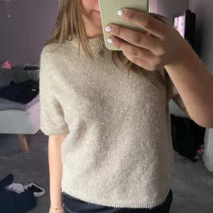 Beige stickad kortärmad topp - Mysig beige stickad topp med korta ärmar och rund hals. Den har en enkel och clean look med ribbade kanter vid ärmslut och nederkant. Den är från Ginatricot i strl M!💞