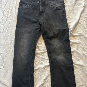 Svarta Lee Luke jeans W34 L32 - Säljer ett par svarta Lee Luke jeans i storlek W34 L32. Jeansen har klassisk femficksdesign, raka ben och är tillverkade i ett slitstarkt bomullsmaterial. Snygg tvätt med lite slitningar för en cool look. Perfekta till din vardagsstil.