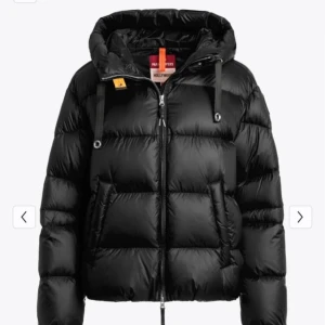 Svart pufferjacka från Parajumpers - Snygg svart pufferjacka från Parajumpers med huva, dragkedja och coola detaljer som logopatch på ärmen och snörning i huvan. Jackan är vadderad och har två stora fickor framtill. Perfekt för kalla dagar när du vill hålla stilen.