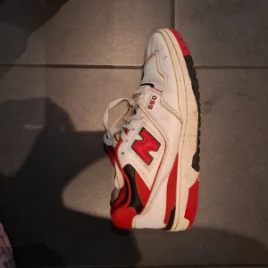 New Balance 550 sneakers röd/vit - Säljer ett par New Balance 550 sneakers i vitt, rött och svart. Skorna har klassisk retrodesign med perforerade paneler, snörning och tydlig New Balance-logga på sidan. Ovandelen är i skinn och textil, sulan är robust och har bra grepp.