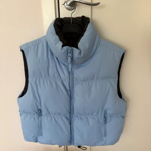 Ljusblå dunväst med hög krage - Snygg ljusblå dunväst med hög krage och dragkedja framtill. Västen har två fickor med dragkedja och en stilren, puffig design. Perfekt för lager-på-lager och ger en cool vibe till din outfit.