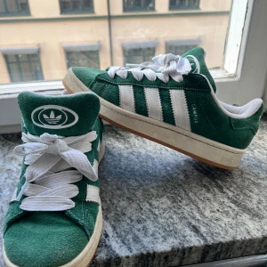 Adidas Campus 00s gröna sneakers stl 40 - Säljer mina gröna Adidas Campus 00s sneakers med klassiska vita ränder och breda vita skosnören. Ovandel i mocka och vit sula med gummidetaljer. Storleken är 40 (unisex). Skorna är i väldigt bra skick, bara använda fåtal gånger! Priset är 400kr, prutat och klart. Först till kvarn!🚀