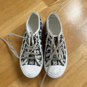 Christian Dior Oblique sneakers - Snygga låga sneakers från Christian Dior med ikoniskt blått och beige oblique-mönster. Skorna har vita snören, rund tå och vit platt sula med Christian Dior-logga på sidan och framtill. Tillverkade i canvas med klassisk stjärndetalj under sulan.