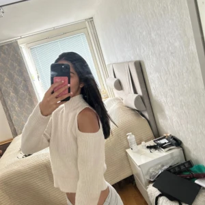 Vit stickad croppad tröja med cut out - Säljer en vit stickad croppad tröja med polokrage och snygga cut out-detaljer på axlarna. Tröjan har lång ärm och ribbade muddar. Perfekt för dig som vill ha en trendig och mysig look till hösten eller vintern.