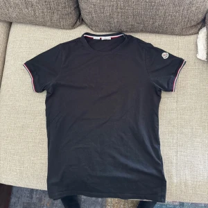 Moncler T-shirt - Klassisk svart Moncler T-shirt i storlek S. T-shirten är i jättebra skick – den har inte tappat färg eller form och ser fortfarande fräsch ut. ✔ Storlek: S ✔ Färg: Svart ✔ Skick: Mycket bra 📦 Skickas inom 24h