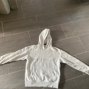 Grå hoodie med tryck från J&J - Snygg ljusgrå hoodie från J&J med stilrent tryck på bröstet. Tröjan har huva, magficka och ribbade muddar vid ärmslut och nederkant. 