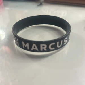 Marcus & Martinus svart armband - Svart silikonarmband med vit text där det står 'Marcus & Martinus'. Perfekt accessoar för fans som vill visa sitt stöd för den norska popduon. Armbandet är flexibelt och bekvämt att bära hela dagen. !!pris kan diskuteras!!