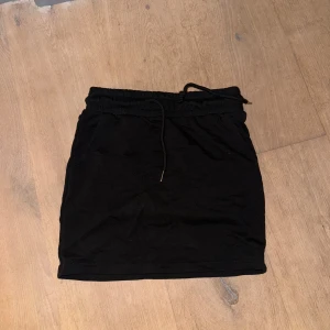 Svart kortkjol från Shein med snörning - Svart kortkjol från Shein med elastisk midja och snörning. Kjolen har fickor på sidorna och är gjord i mjuk bomullsmix. Enkel och clean design som är lätt att matcha med olika toppar.