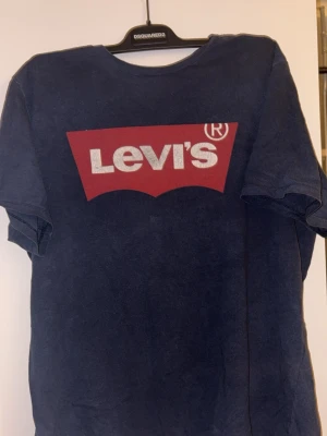 Mörkblå Levi's t-shirt XL - Snygg mörkblå t-shirt från Levi's i bomull med klassiskt rött och vitt logotryck på bröstet. T-shirten har korta ärmar och rund hals. Perfekt för en chill och avslappnad stil. Levi's-märke på ärmen för extra detalj.