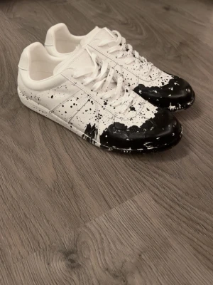 Maison Margiela - Maison Margiela sneakers i vitt skinn med svart paint splatter. Dom är helt nya och storlek 46. Skobox ingår ej. 
