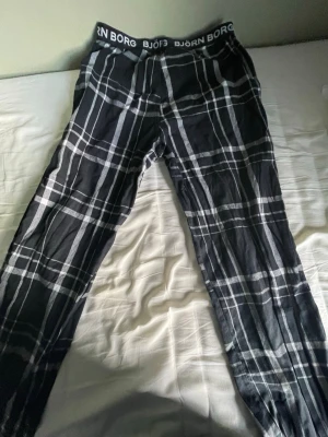 Svarta rutiga byxor från Björn Borg - Säljer ett par svarta byxor från Björn Borg med vitt rutmönster och bred resår i midjan med logga. Byxorna är raka i secret och har en avslappnad passform. Perfekta för chill dagar hemma eller som mjukisbyxor.