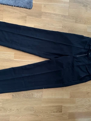 Svarta kostymbyxor från Ciszere M - Snygga svarta kostymbyxor från Ciszere i storlek M. Klassisk rak passform med pressveck och dragkedja i midjan. Perfekta till en stilren look och tillverkade i ett mjukt, välsittande material.