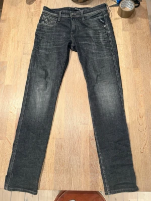 Replay Anbass slim fit jeans svart - Säljer ett par Replay Anbass slim fit jeans i svart tvätt med snygga slitningar. Klassisk femficksmodell med Replay-logga på fickan och kontrastsömmar. Jeansen är tillverkade i bomull med en skön stretch för extra komfort.