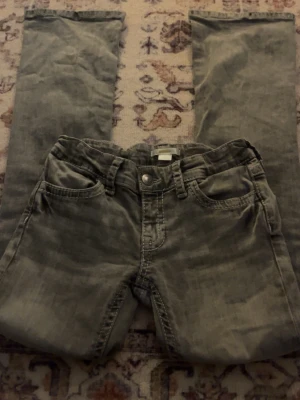 Grå jeans från Gina Tricot - Säljer ett par grå jeans från Gina Tricot i storlek 152. Byxorna har raka ben, klassisk femficksdesign och dekorativa sömmar på fickorna. Tillverkade i slitstarkt bomullsmaterial och har knapp- och dragkedjestängning framtill.