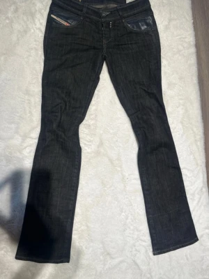 Diesel Rokket vintage low waist svarta jeans med skinn - Säljer ett par svarta Diesel Rokket jeans med snygga detaljer i svart skinn på fickorna. Jeansen har klassisk femficksdesign med en låg midja. Supersnygga. Pris kan diskuteras😊