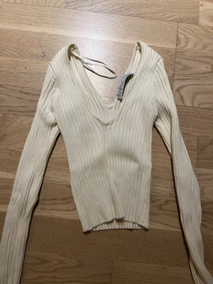 Ribbad v-ringad topp från Bershka - Säljer en ljusbeige ribbad topp från Bershka med lång ärm och djup v-ringning. Toppen är croppad och har en slim passform som sitter snyggt på kroppen. Perfekt att styla med höga jeans eller kjol.