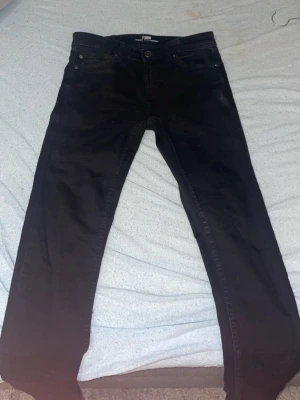 Svarta jeansbyxor från FSBN 28/32 - Svarta jeansbyxor från FSBN med klassisk femficksdesign och raka ben. Byxorna har normal passform och är tillverkade i ett mjukt bomullsmaterial med lite stretch. Perfekta för dig som gillar en enkel och clean look.