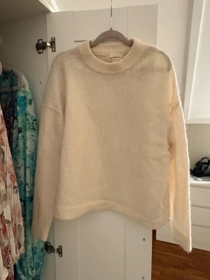 Beige stickad tröja med rund hals - Mysig beige stickad tröja med rund halsringning och ribbade muddar. Tröjan har en relaxed passform och långa ärmar, perfekt för lager på lager under kyliga dagar. Enkel och stilren design som funkar till allt.