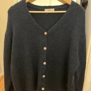 Mörkblå kofta från Gina Tricot - Mysig mörkblå kofta från Gina Tricot med v-ringning och fem knappar framtill. Koftan har en loose passform och är stickad i ett fluffigt material som känns riktigt skönt. Perfekt för lager på lager under kyliga dagar.