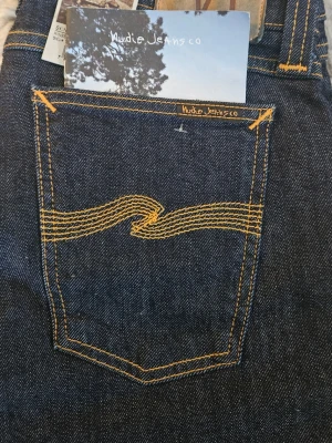 Nudie Jeans Skinny Lin W30 L32 - Mörkblå skinny jeans från Nudie Jeans, modell Skinny Lin. Klassisk femficksdesign med orange kontrastsömmar och ikonisk broderad bakficka. Tillverkade i ekologisk bomull med stretch för en tight passform. Perfekta för dig som gillar en smal siluett.