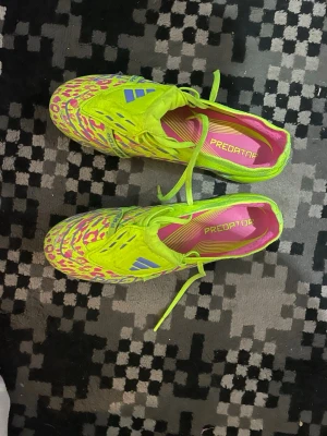 Adidas Predator fotbollsskor neon - Säljer ett par Adidas Predator fotbollsskor i neon-gul färg med rosa och blå detaljer samt leopardmönster. Skorna har snörning, låg profil och är tillverkade i syntetmaterial. Perfekta för dig som vill sticka ut på planen!