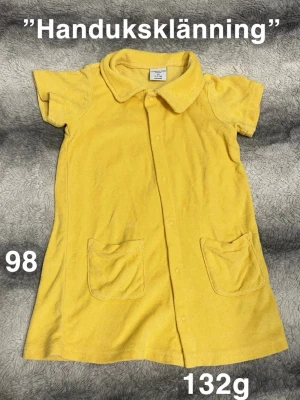 Gul handduksklänning med fickor - Söt gul handduksklänning från Polarn o pyret i storlek 98. Klänningen har korta ärmar, krage, knappar framtill och två praktiska fickor. Perfekt för sommardagar på stranden eller efter badet. frotté.🌸 Fint använt skick. Storlek 98