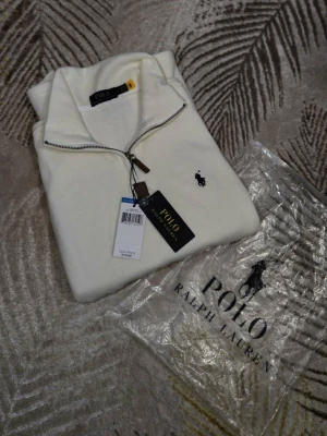 Vit half zip tröja Polo Ralph Lauren - Säljer en stilren vit tröja från Polo Ralph Lauren med half zip och klassisk broderad logga på bröstet. Tröjan är i bomull och har en mjuk känsla, perfekt för lager på lager. Passar dig som gillar enkel men snygg design.
