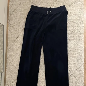 Mörkblå mjukisbyxor Juicy Couture M - Mörkblå mjukisbyxor från Juicy Couture i mjuk sammet. Byxorna har bred resår i midjan med snörning, stora fickor fram och bak med knappdetaljer samt diskret JC-logga på ena fickan. 
