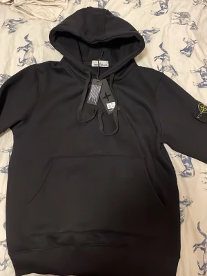 Hoodi från Stone Island  - Svart Stone Island hoodie i mycket fint skick. Tjock och bekväm kvalitet, perfekt för vardagsbruk och kallare väder. Klassisk och stilren design med original Stone Island badge på ärmen.