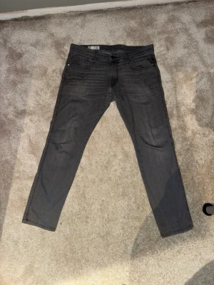 Replay Anbass grå jeans, storlek 34 - Säljer ett par Replay Anbass jeans i snygg mörkgrå tvätt. Modellen har klassisk femficksdesign, raka ben och diskreta sömmar. Jeansen är tillverkade i mjukt och stretchigt jeansmaterial för skön passform. 