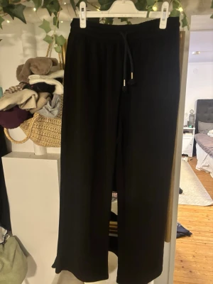 Svarta mjukisbyxor med snörning M - Säljer ett par svarta mjukisbyxor i storlek M. Byxorna har resår i midjan och snörning med metalländar. De har en loose passform och raka ben, perfekta för chill dagar eller när du vill vara bekväm.