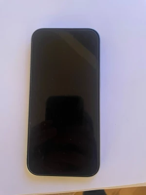iPhone 15 - Snygg iPhone 15 i vitt med dubbla kameror. Skärmen och baksidan ser ut att vara i mycket gott skick utan synliga repor eller skador. Perfekt för dig som vill ha en modern och kraftfull smartphone med hög prestanda och bra kamera.