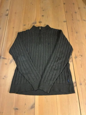 Mörkgrå stickad limited tröja Yves Dorsey - Mörkgrå kabelstickad tröja från Yves Dorsey med ribbad hög krage och half zip-dragkedja. Klassisk och chunky look med långa ärmar och diskret logga på bröstet. Perfekt för kyliga dagar och enkel att styla till jeans.Original inköpt för 99.99€.