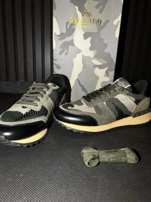 Valentino Garavani Rockrunner sneakers camo - Snygga Valentino Garavani Rockrunner sneakers i camouflage med gröna, svarta och beige toner. Bakdel i mocka, mesh och skinn med coola nitar på hälen. Klassisk snörning och robust sula. Perfekta för dig som vill sticka ut med lyxig streetstyle.