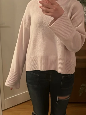 Ljusrosa stickad tröja med vida ärmar - Mysig ljusrosa stickad tröja med breda, långa ärmar och ribbade muddar vid ärmslut och nederkant. Tröjan har en avslappad passform och rund halsringning. Perfekt för dig som gillar en enkel men ändå trendig look. Vet inte vilken storlek men passar perfekt på mig som brukar ha xs eller s i tröjor. Pris går att diskuteras!