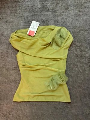 Grön  axelbandslös blus med volanger - Trendig grön axelbandslös blus med draperad design och dekorativa volangdetaljer i tyll på brösten. Det är storlek S men kan passa XS