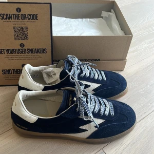 MOA Concept sneakers i blå mocka - Snygga sneakers från MOA Concept i mörkblå mocka med vita detaljer och coolt blixtmönster på sidan. Skorna har vit häl, mönstrade snören och en genomskinlig gummisula. Perfekta för dig som gillar streetstyle och vill sticka ut lite extra. Skorna är oanvända och har allt OG med sig och hör av dig ifall du undrar något 👍